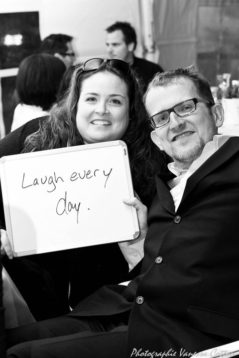 Robert Pearson and his wife holding up a sign that says Laugh every day